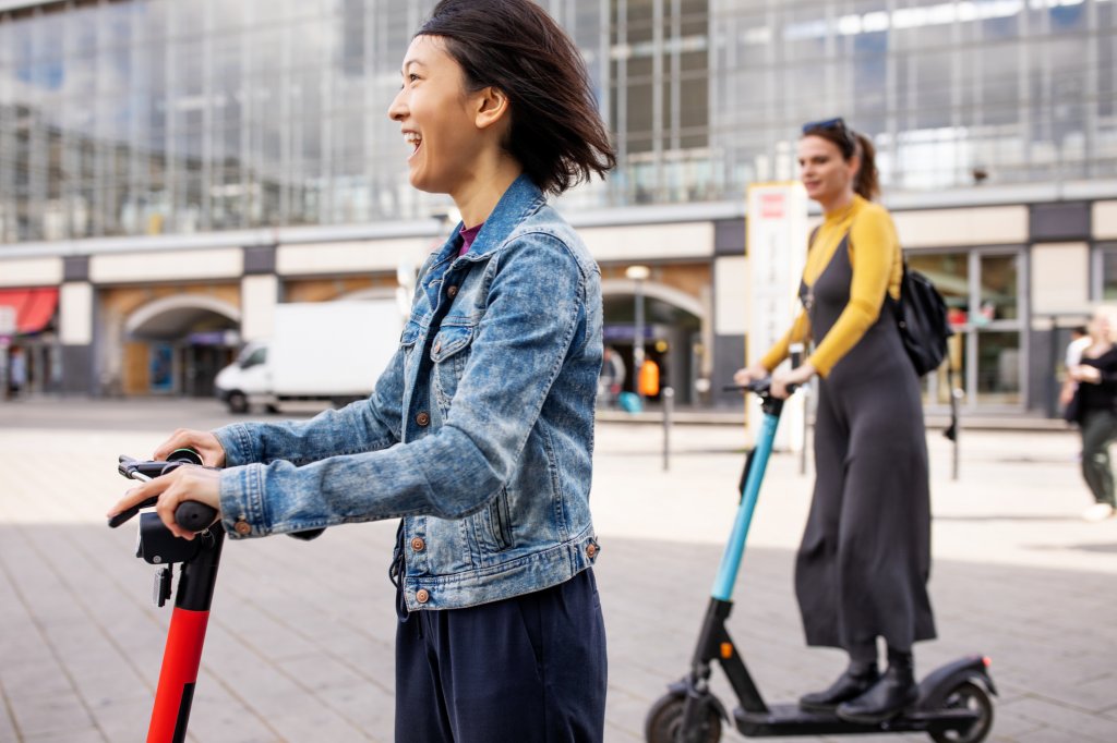 Cheerful woman riding push scooter on street in city during vacation.