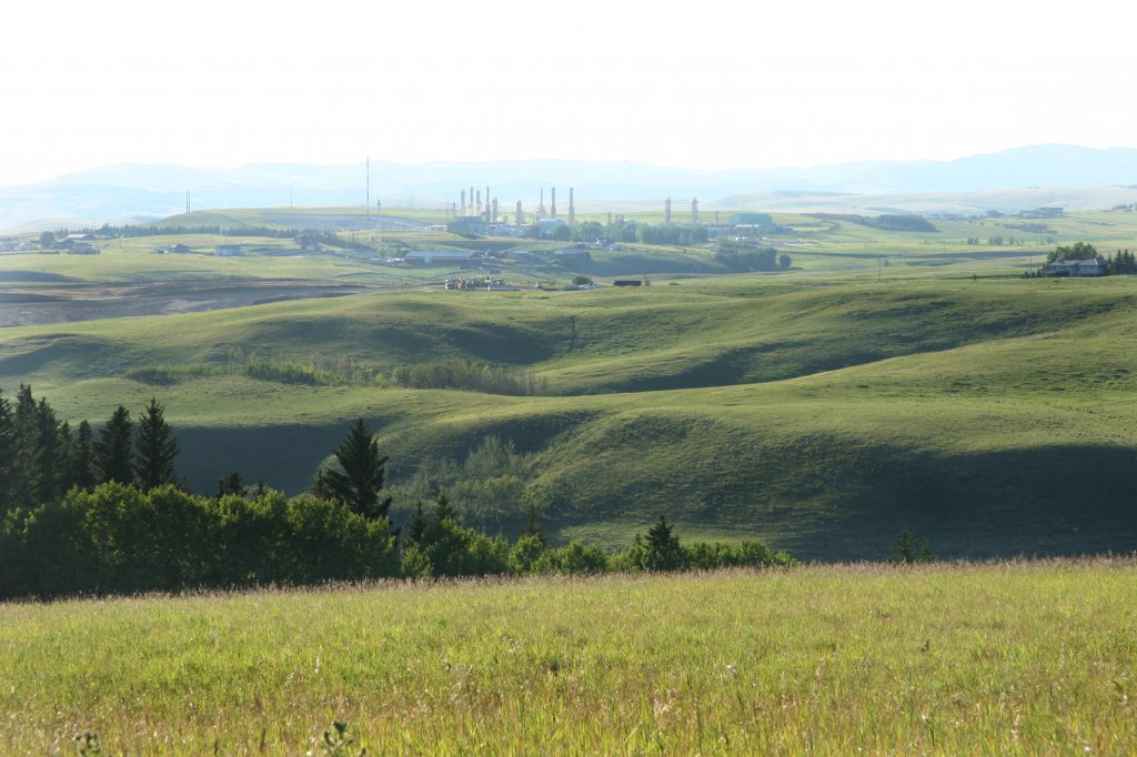 Oil refinery Gas plant in distance with rolling green Foothills in Foreground.